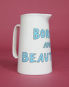 White pitcher with blue text 'BORN AND BEAUTIFUL' on a pink background
