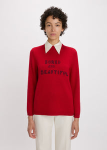 Person wearing a red sweater with text, white shirt, and beige pants on a white background