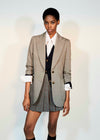 A model wearing a tailored pinstripe blazer over a white collared shirt and dark vest, paired with a matching pleated mini skirt, photographed against a plain light background.