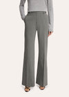 A model stands against a light studio background wearing a tailored light gray pinstripe suit with a white shirt, patterned tie, and black pointed shoes.