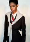 A model wearing a dark brown textured blazer over a white collared shirt with a red and gray striped tie, styled with a light gray knit wrap draped over the shoulders.